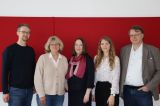 Fünf Personen stehen nebeneinander vor einer roten Wand.
